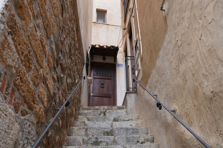 A set of grey concrete stairs leading up to a dark blue front door with a glass pane divided into smaller sections on a building with grey stone exterior walls. The stairs are enclosed by black metal 
