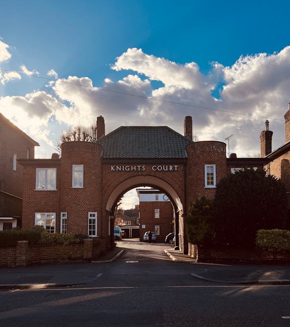 The image depicts the entrance to a residential property named Knights Court, constructed from red brick with a prominent arched gateway through which a parking area is visible. The gateway is flanked